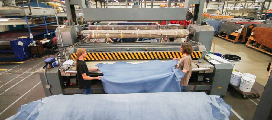 Two leather manufacturing workers move hides off a heat embosser.