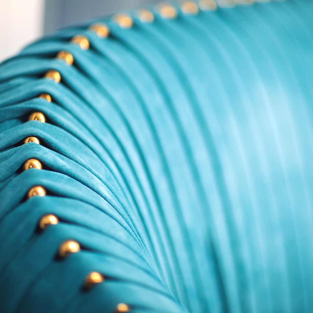 A blue sued sofa is upholstered with brass features.