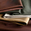 Cortina Leathers Linden full grain collection hero photo shows naked aniline leather hides in rich browns flanking a moss green, a pearl white and a buttery yellow, showcased with deep shadows to highlight the pure aniline tonal variation and natural markings.